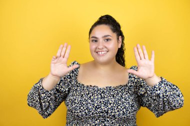 Sarı arka planda kıvırcık saçları olan genç ve güzel bir kadın dokuz numaralı parmaklarıyla gülümseyerek kendinden emin ve mutlu olduğunu gösteriyor.