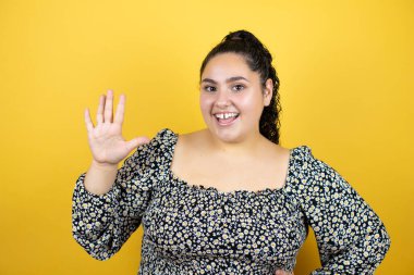Sarı arka planda kıvırcık saçları olan genç ve güzel bir kadın beş numaralı parmaklarıyla gülümseyerek kendinden emin ve mutlu olduğunu gösteriyor.