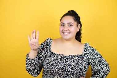 Sarı arka planda kıvırcık saçları olan genç ve güzel bir kadın dört numaralı parmaklarıyla gülümseyerek kendinden emin ve mutlu olduğunu gösteriyor.