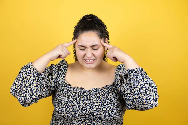 ストレスが原因で頭の中で痛みのために頭の上に手で隔離された黄色の背景に巻き毛を持つ若い美しい女性 片頭痛に苦しむ — ストック写真
