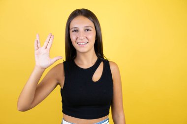 İzole edilmiş sarı arka planda güzel bir kız çocuğu Star Trek ucube sembolü yapıyor.