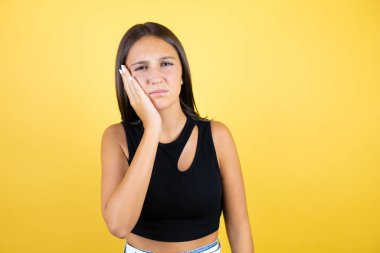 Güzel bir kız çocuğu, izole edilmiş sarı arka planda diş ağrısı ya da diş hastalığından dolayı acı dolu bir ifadeyle ağıza dokunuyor.