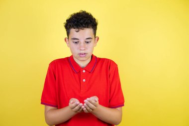 Güzel genç bir çocuk, izole edilmiş sarı arka planda avuçlarıyla gülümsüyor, el hareketi yapıyor. Tutun ve koruyun