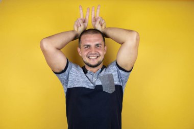 Sarı arka planda dikilen Rus adam komik ve çılgın pozlar veriyor. Parmakları kafasında tavşan kulağı, neşeli bir gülümseme.