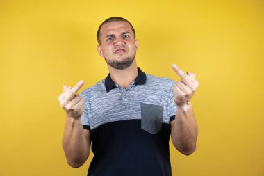 Russian man standing over insolated yellow background showing middle finger doing fuck you bad expression, provocation and rude attitude. screaming excited