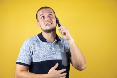 Sarı arka plan üzerinde duran Rus adam şaşırmış bir yüzle akıllı telefon kullanarak sohbet ediyor..