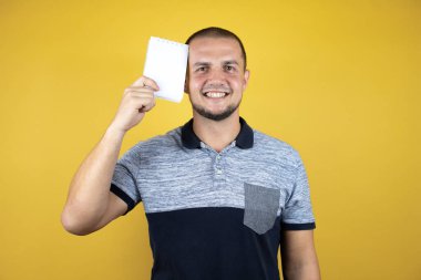 Rus adam sarı arka planda durmuş gülümsüyor ve elinde boş bir defter gösteriyordu.