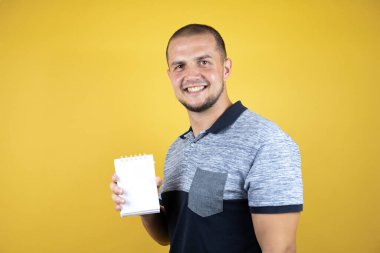 Rus adam sarı arka planda durmuş gülümsüyor ve elinde boş bir defter gösteriyordu.