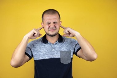 Rus adam sarı arka planda dikiliyor. Yüksek sesli müziğin gürültüsü için parmaklarıyla kulakları kapatıyor. Sağır kavramı.