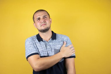 Omzunda ağrı ve acı dolu bir ifadeyle sararmış sarı arka planda duran Rus bir adam.