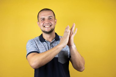 Rus adam sarı arka planda ayakta alkışlıyor ve alkışlıyor mutlu ve neşeli, gururla gülümsüyor.