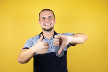 Rus adam izole edilmiş sarı arka planda dikiliyor. Baş parmaklarını yukarı aşağı hareket ettiriyor. Anlaşmazlık ve uzlaşma ifadesi. Çılgın çatışma