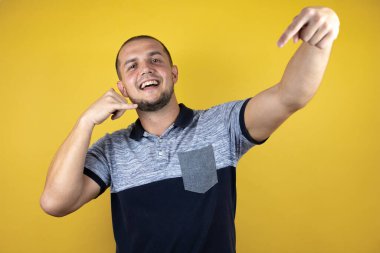 Rus adam sarı arka planda durmuş gülümsüyor telefonla el ve parmaklarıyla hareket ediyor telefonda konuşuyor ve elini işaret ediyor.