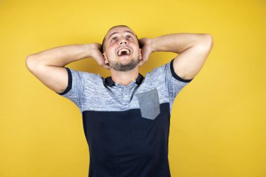 Rus adam sarı arka planda duruyor rahatlıyor ve esniyor, kolları ve elleri başının arkasında mutlu bir şekilde gülümsüyor.