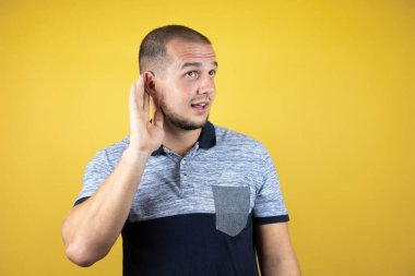 Sarı arka planda dikilen Rus adam bir söylenti ya da dedikoduyu dinlerken sırıtıyor. Sağırlık kavramı.