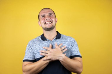 Sarı arka planda dikilen Rus adam elleri göğsünde ve yüzünde minnet dolu bir jest ile gülümsüyor..