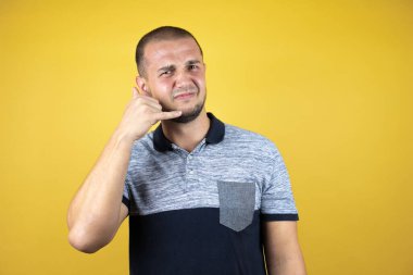 Rus adam sarı arka planda durmuş gülümsüyor telefonla el ve parmaklarıyla jest yapıyor telefonda konuşuyor gibi.