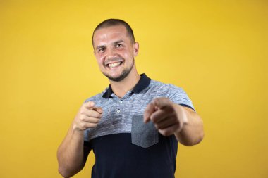 İzole edilmiş sarı arka planda dikilen Rus adam mutlu ve komik yüzüyle kamerayı işaret ediyor. İyi enerji ve titreşimler.