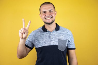 Mutlu ve kendinden emin bir şekilde gülümserken iki numarayı göstererek..