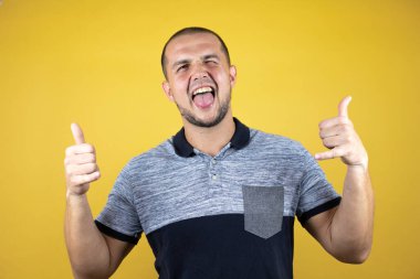 Rus adam sarı arka planda duruyor çılgın bir ifadeyle bağırıyor elleri havada rock sembolü yapıyor.