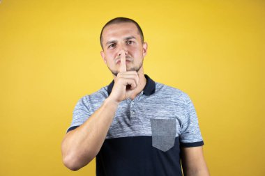 Rus adam izole edilmiş sarı arka planda duruyor ve parmakları dudaklarında sessiz olmak istiyor. Sessizlik ve gizli konsept.