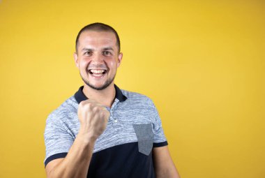 Sarı arka planda dikilen Rus adam mutlu ve heyecanlı bir şekilde kollarını kaldırıp, gülümseyip başarı için haykırıyor..