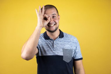 Rus adam sarı arka planda dikiliyor. Şaşırmış yüz ifadesiyle şaşırmış, parmaklarının arasından bakıyor.