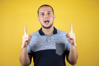 İzole edilmiş sarı arka plan üzerinde duran Rus adam şaşırmış ve şaşırmıştı. Parmaklarıyla yukarı bakıyor ve kollarını kaldırıyordu.