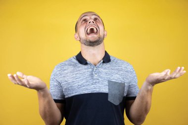 İzole edilmiş sarı arka planda dikilen, elleri ve kolları havada, kafası karışmış bir Rus adam.