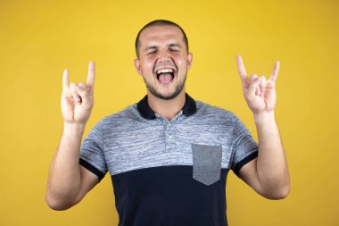 Rus adam izole edilmiş sarı arka planda duruyor çılgın bir ifadeyle bağırıyor elleri havada rock sembolü yapıyor. Müzik yıldızı. Ağır konsept.