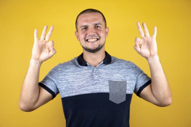 İzole edilmiş sarı arka planda dikilen Rus adam gülümsüyor iki elinde ve parmaklarıyla 