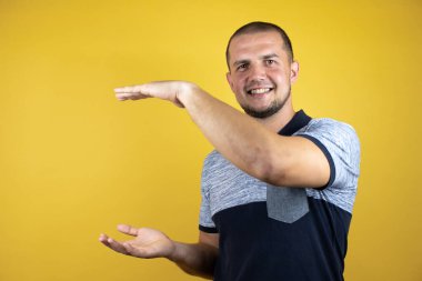 Sararmış arka planda dikilen Rus adam büyük ve büyük boyut işareti, ölçü sembolü gösteren elleriyle şaşırmış ve el kol hareketi yapıyordu.