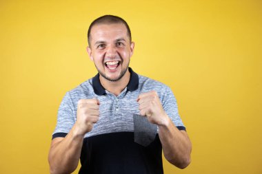 Sarı arka planda dikilen Rus adam mutlu ve heyecanlı bir şekilde kolları havada, gülümseyen ve başarı çığlıkları atan kazanan bir jest yapıyor. Kutlama konsepti.