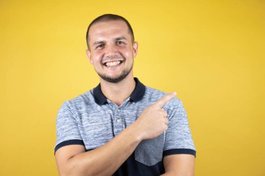 Rus adam sarı arka planda dikiliyor gülümsüyor ve başparmağını kaldırıyor..