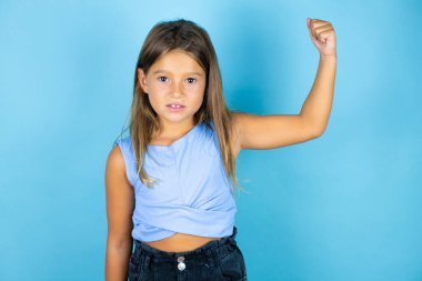 İzole edilmiş mavi arka planda genç ve güzel bir kız. Kollarında gururla gülümseyen kaslar var.