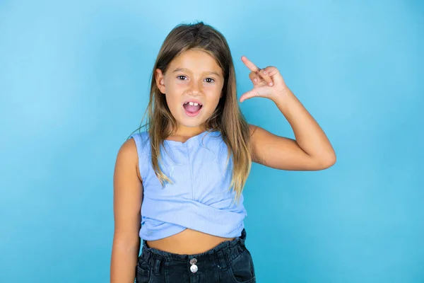 年轻美丽的小女孩在孤零零的蓝色背景上微笑着 自信地摆出姿势 手做着小尺寸的手势 手指看着镜头 计量概念 — 图库照片