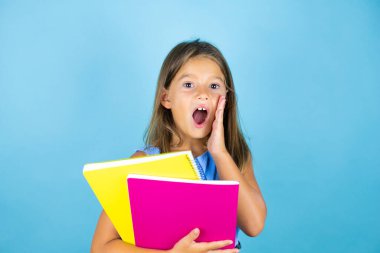 Genç, güzel kız öğrenci elinde not defteriyle izole edilmiş mavi arka planda elleri ağızda bağırıyor ve çığlıklar atıyordu.