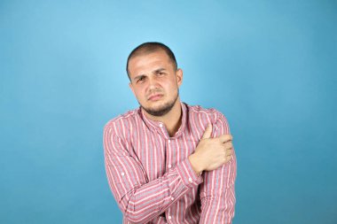 Rus iş adamı mavi arka planda kırmızı tişört giyiyor. Omzunda ağrı ve acı dolu bir ifade var.