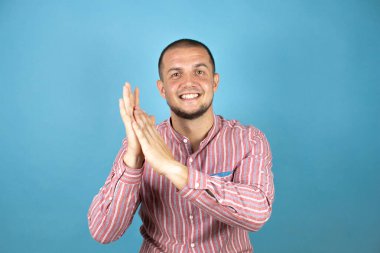 Rus iş adamı mavi arka planda kırmızı tişört giyip alkışlıyor ve mutlu, neşeli ve gururlu elleri bir arada alkışlıyor.