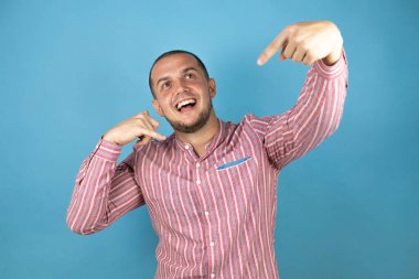 Rus iş adamı mavi arka planda kırmızı gömlekli, gülümseyen, el ve parmaklarıyla telefon hareketi yapan telefonda konuşan ve elini işaret eden biri.