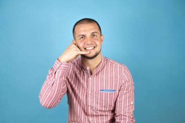 Rus iş adamı mavi arka planda kırmızı bir gömlek giyip gülümsüyor telefonla el ve parmaklarıyla jest yapıyor telefonda konuşuyor gibi.