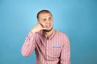 Rus iş adamı mavi arka planda kırmızı bir gömlek giyip gülümsüyor telefonla el ve parmaklarıyla jest yapıyor telefonda konuşuyor gibi.