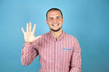 Rus iş adamı mavi arka planda kırmızı tişört giyer ve beş numarayı gösterirken kendinden emin ve mutlu bir şekilde gülümserdi..