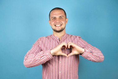 Rus iş adamı mavi arka planda gülümsüyor. Elleriyle kalp sembolü ve şekli gösteriyor. Romantik konsept.