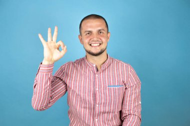 Mavi arka planda gülümseyen bir Rus iş adamı el ve parmaklarıyla imza atarken iyi iş çıkarıyor. Başarılı ifade