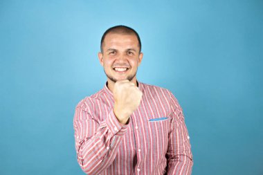 Rus iş adamı mavi arka planda çok mutlu ve heyecanlı. Kollarını kaldırmış, gülümseyen ve başarı için çığlık atan kazanan bir jest yapıyor..