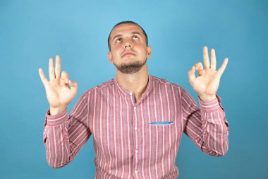 Rus iş adamı mavi arka planda rahatlayıp gözleri kapalı parmaklarıyla meditasyon hareketi yaparken gülümsüyor. Yoga konsepti.