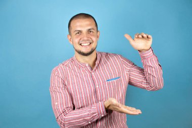 Rus iş adamı mavi arka planda şaşırdı ve elleri ile büyük ve büyük boy işareti, ölçü sembolü gösteren hareketler yaptı