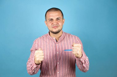 Rus iş adamı mavi arka planda çok mutlu ve heyecanlı bir şekilde kollarını kaldırıp, gülümseyip, başarı için bağırarak kazanan jestler yapıyor. Kutlama konsepti.