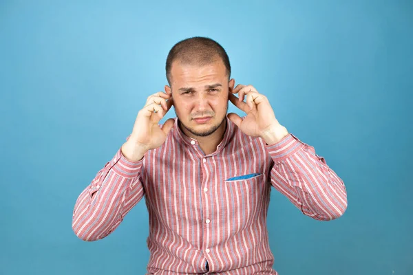Rus iş adamı mavi arka planda kırmızı gömlek giyiyor. Yüksek sesli müzik sesi için kulaklarını parmaklarıyla kapatıyor. Sağır kavramı.